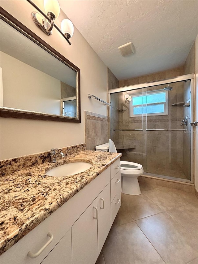 bathroom featuring toilet, tile patterned flooring, an enclosed shower, a textured ceiling, and vanity