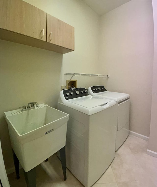 clothes washing area with light tile patterned floors, cabinets, washer and clothes dryer, and sink