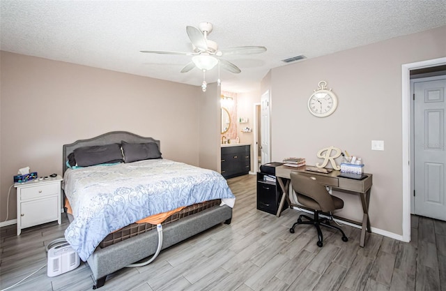 bedroom with light wood-type flooring, ceiling fan, a textured ceiling, and connected bathroom