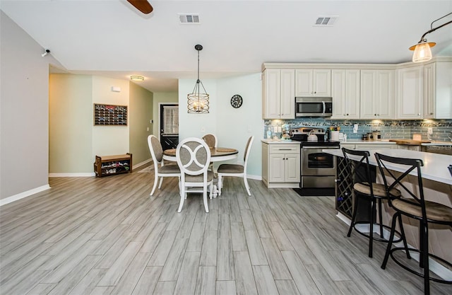 kitchen featuring pendant lighting, tasteful backsplash, stainless steel appliances, and light wood-type flooring