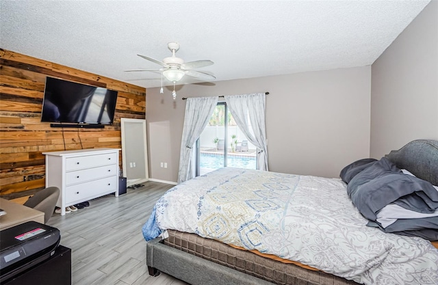 bedroom with access to exterior, a textured ceiling, light hardwood / wood-style flooring, and wood walls