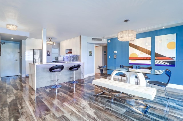 kitchen with pendant lighting, stainless steel fridge, dark hardwood / wood-style flooring, a kitchen bar, and kitchen peninsula