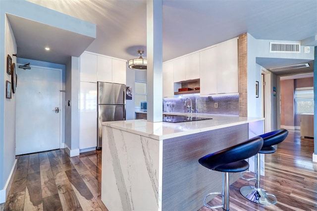 kitchen with stainless steel refrigerator, backsplash, a kitchen breakfast bar, kitchen peninsula, and white cabinets