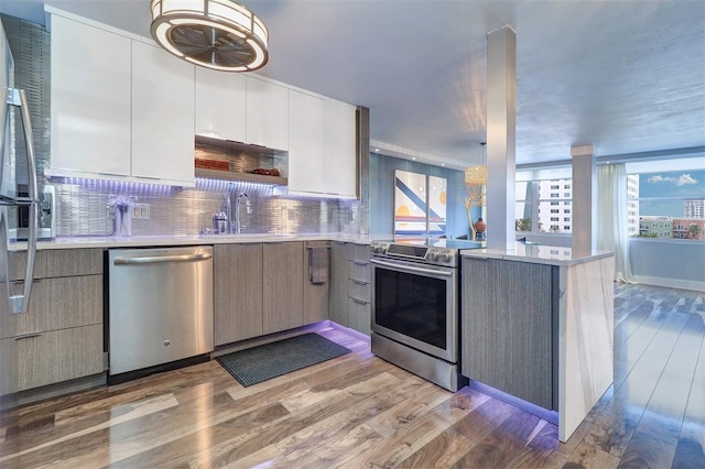 kitchen with sink, dark wood-type flooring, stainless steel appliances, white cabinets, and decorative backsplash