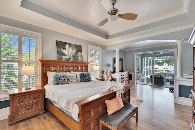 bedroom featuring ceiling fan, ornamental molding, a raised ceiling, and decorative columns