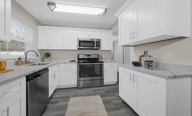 kitchen with sink, appliances with stainless steel finishes, white cabinetry, dark hardwood / wood-style floors, and light stone counters