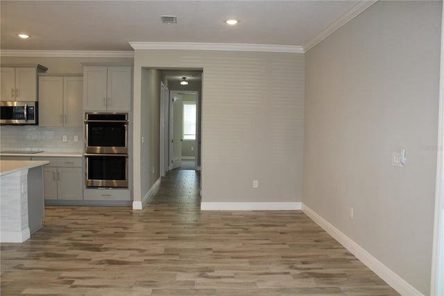 kitchen featuring stainless steel appliances, ornamental molding, light wood-type flooring, backsplash, and gray cabinets