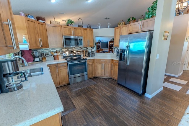 kitchen featuring dark wood-type flooring, sink, light stone counters, stainless steel appliances, and backsplash