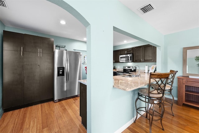 kitchen featuring a kitchen bar, light wood-type flooring, appliances with stainless steel finishes, dark brown cabinets, and sink