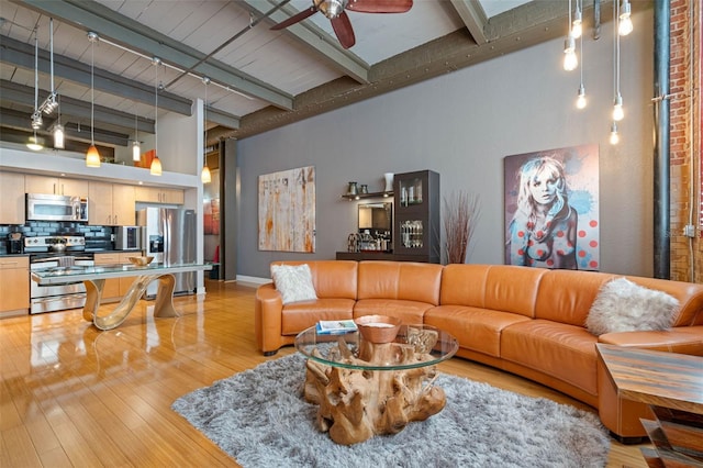 living room with light hardwood / wood-style flooring, track lighting, a towering ceiling, ceiling fan, and beamed ceiling