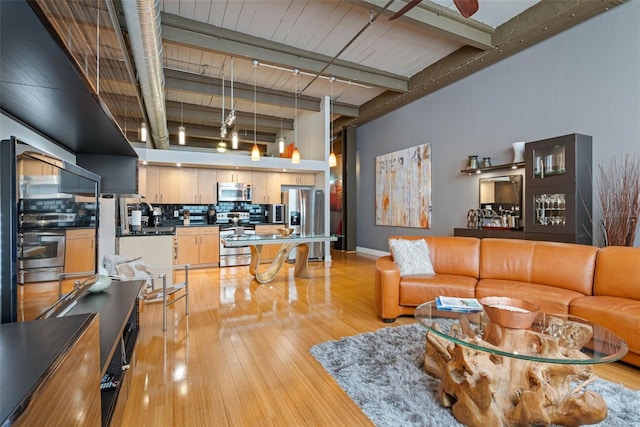 living room with beamed ceiling, light wood-type flooring, ceiling fan, a high ceiling, and rail lighting