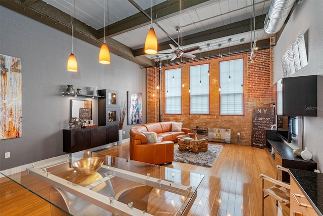 living room featuring brick wall, ceiling fan, plenty of natural light, hardwood / wood-style flooring, and beam ceiling