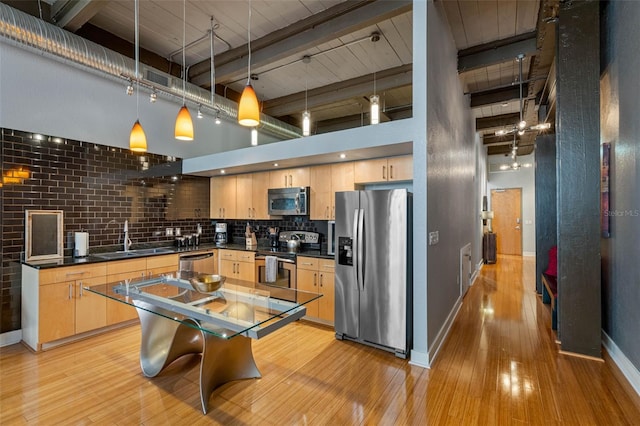 kitchen featuring stainless steel appliances, sink, a towering ceiling, light brown cabinets, and hanging light fixtures