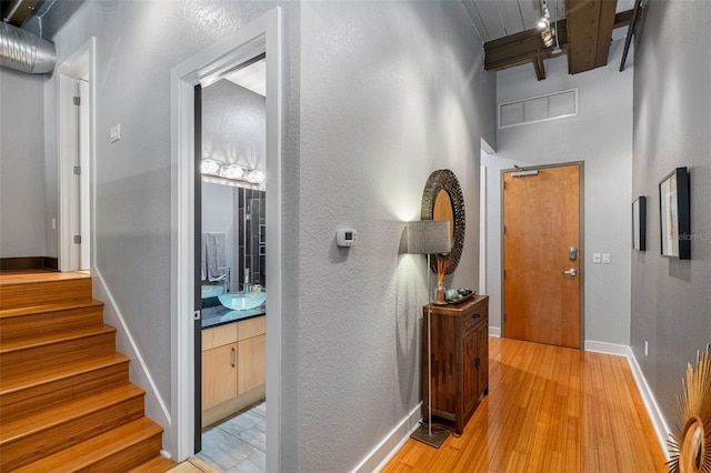 hallway with light hardwood / wood-style floors, sink, and beam ceiling