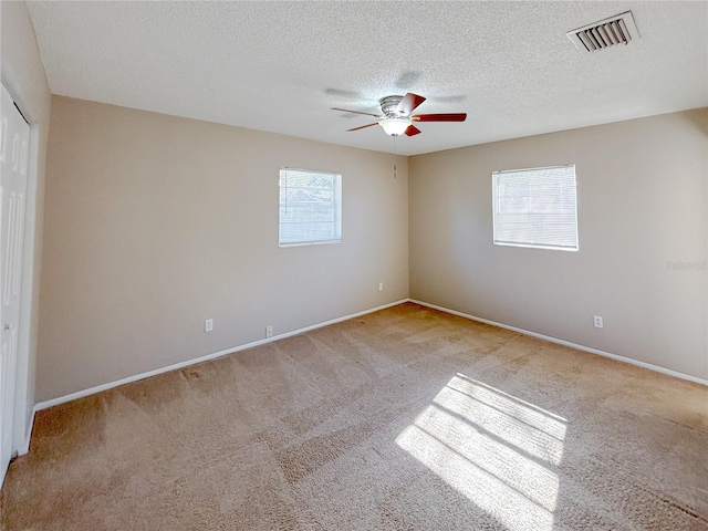 carpeted spare room with a textured ceiling, ceiling fan, and a healthy amount of sunlight