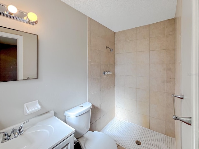 bathroom with a textured ceiling, a tile shower, vanity, and toilet