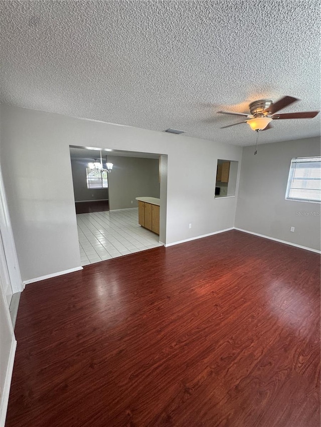 spare room with ceiling fan with notable chandelier, a textured ceiling, and light hardwood / wood-style flooring