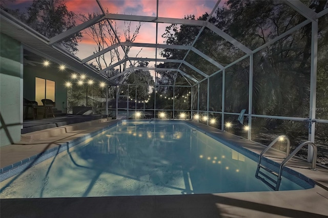 pool at dusk featuring glass enclosure and a patio area