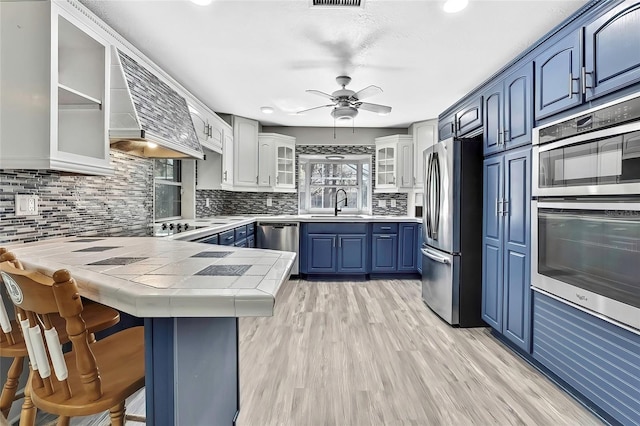 kitchen featuring appliances with stainless steel finishes, tasteful backsplash, kitchen peninsula, a breakfast bar, and blue cabinets