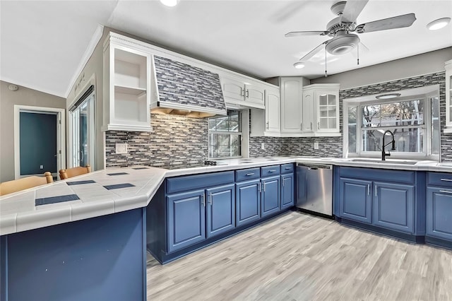 kitchen featuring white cabinets, dishwasher, wall chimney exhaust hood, sink, and blue cabinets