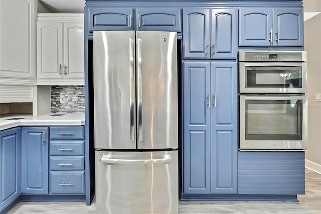 kitchen with backsplash, light hardwood / wood-style floors, blue cabinetry, stainless steel appliances, and tile counters