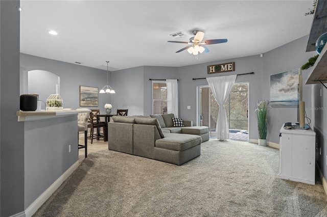 carpeted living room featuring ceiling fan with notable chandelier