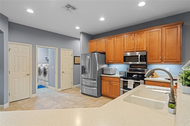 kitchen featuring sink, stainless steel appliances, light tile patterned flooring, and washing machine and clothes dryer