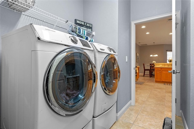 washroom featuring washer and dryer, an inviting chandelier, and light tile patterned floors