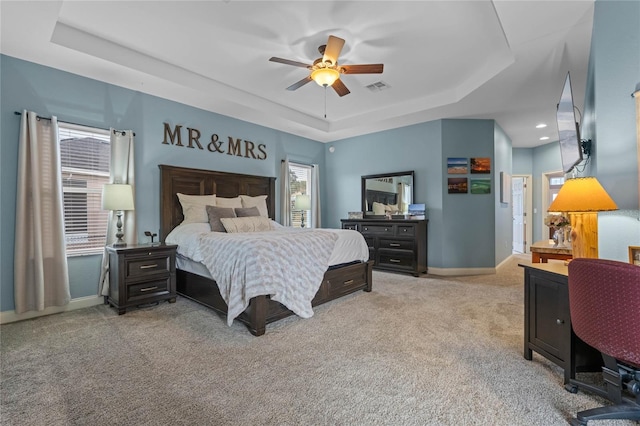 carpeted bedroom with ceiling fan and a raised ceiling