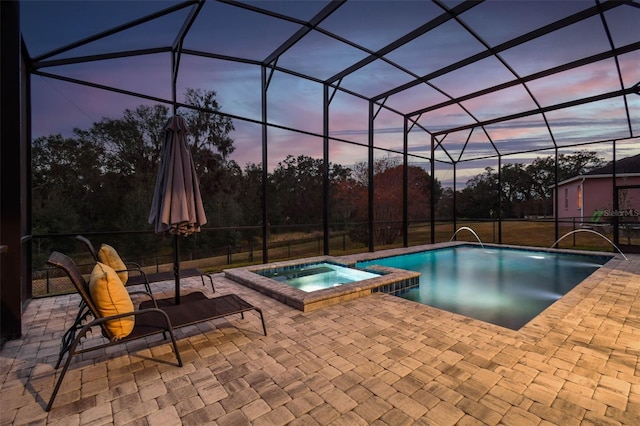 pool at dusk with an in ground hot tub, glass enclosure, and a patio