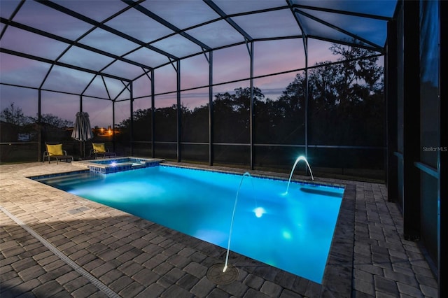 pool at dusk with a patio, pool water feature, glass enclosure, and an in ground hot tub