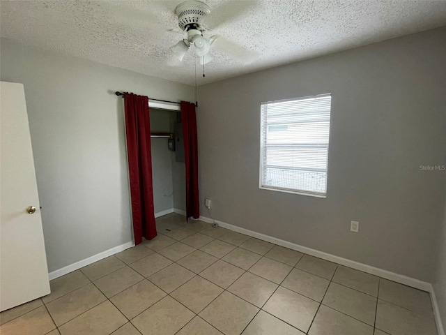 unfurnished bedroom featuring ceiling fan, light tile patterned floors, a textured ceiling, and a closet