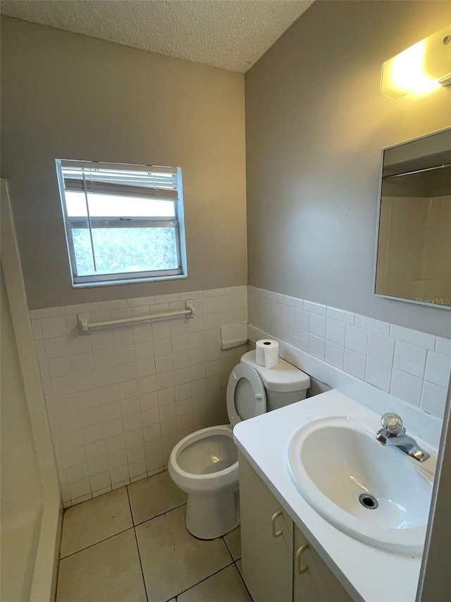 bathroom featuring vanity, tile patterned flooring, toilet, a textured ceiling, and tile walls