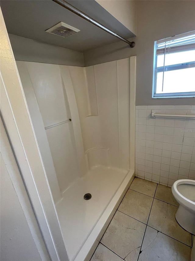 bathroom featuring toilet, a shower, tile patterned floors, and tile walls