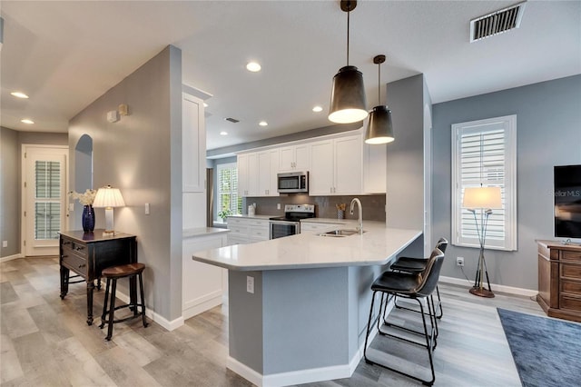 kitchen featuring decorative light fixtures, white cabinetry, stainless steel appliances, sink, and kitchen peninsula