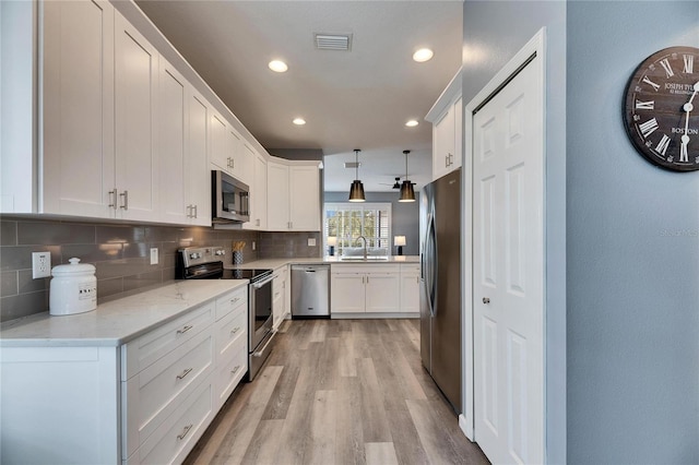 kitchen featuring appliances with stainless steel finishes, white cabinetry, decorative backsplash, sink, and hanging light fixtures