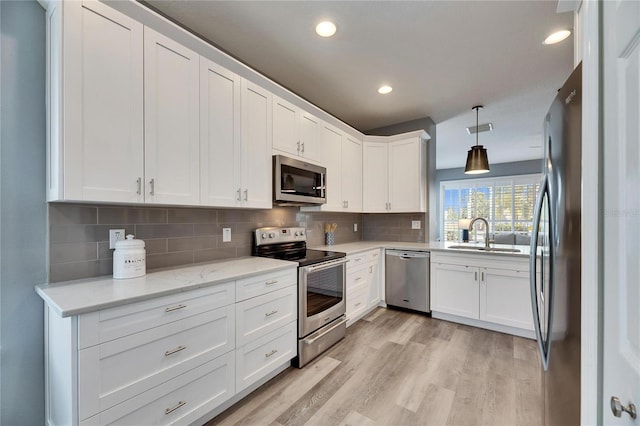 kitchen with backsplash, pendant lighting, sink, white cabinetry, and stainless steel appliances