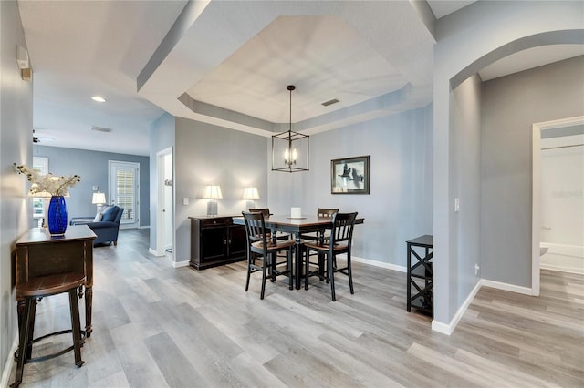 dining room featuring a tray ceiling, light hardwood / wood-style flooring, and a chandelier