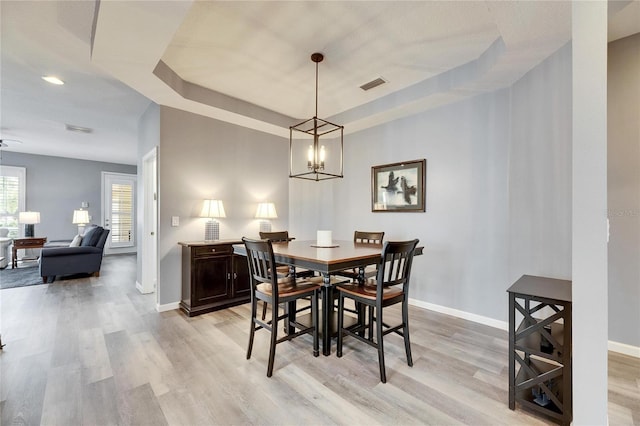 dining space featuring a raised ceiling, ceiling fan with notable chandelier, and light hardwood / wood-style flooring