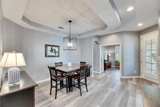 dining space featuring light wood-type flooring, a raised ceiling, and a notable chandelier