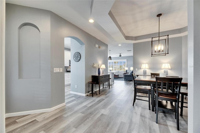 dining area featuring light wood-type flooring, a tray ceiling, and ceiling fan with notable chandelier