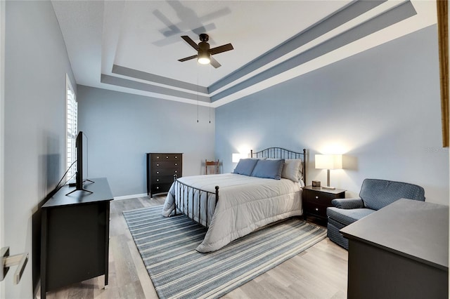 bedroom with ceiling fan, light hardwood / wood-style floors, and a raised ceiling