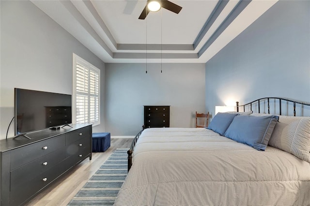 bedroom with a raised ceiling, ceiling fan, and light hardwood / wood-style flooring