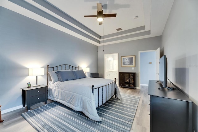 bedroom with ceiling fan, a raised ceiling, ensuite bath, a towering ceiling, and light hardwood / wood-style flooring