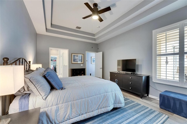 bedroom with ceiling fan, a tray ceiling, light hardwood / wood-style flooring, a spacious closet, and a closet