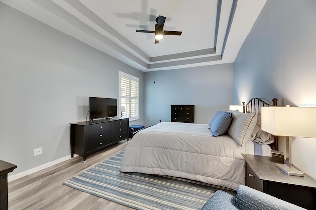 bedroom featuring ceiling fan, light hardwood / wood-style flooring, and a tray ceiling