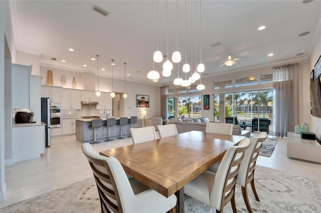 dining room with light tile patterned floors, sink, ceiling fan with notable chandelier, and ornamental molding