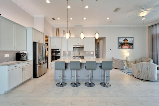 kitchen featuring pendant lighting, stainless steel appliances, decorative backsplash, light stone counters, and a center island with sink