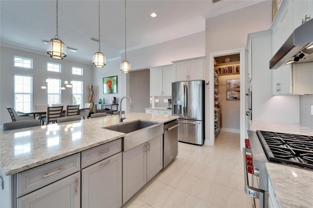 kitchen featuring light stone countertops, appliances with stainless steel finishes, hanging light fixtures, and an island with sink