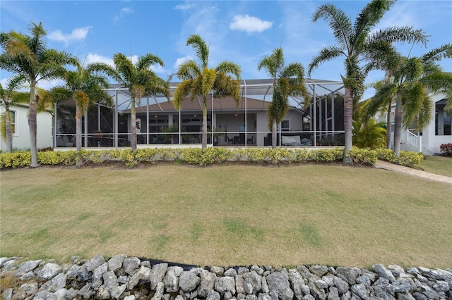 rear view of house featuring glass enclosure and a lawn